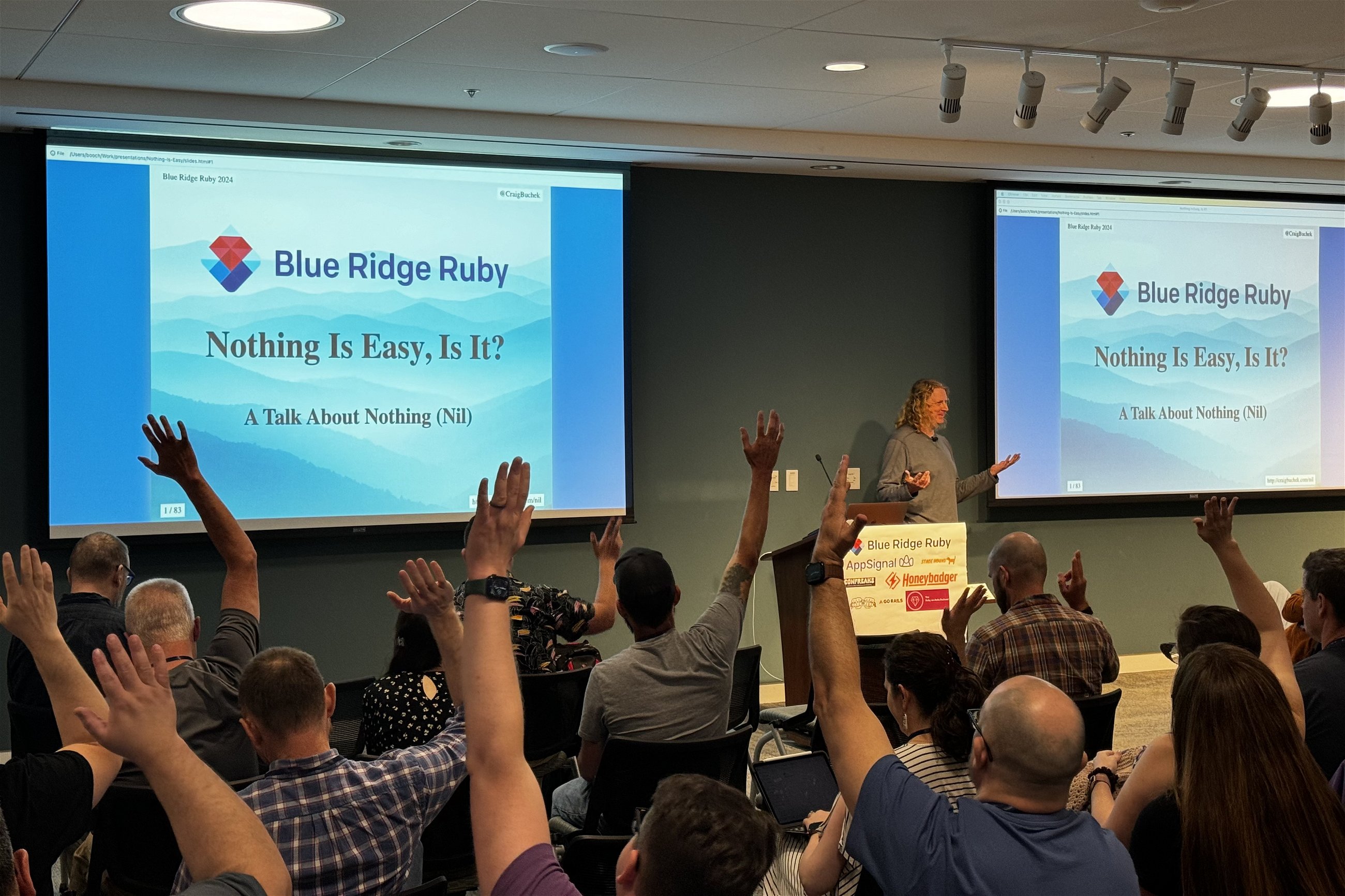 Craig Buchek engaging with the audience during a presentation titled "Nothing Is Easy, Is It? A Talk About Nothing (Nil)" at Blue Ridge Ruby conference, with several attendees raising their hands in response.