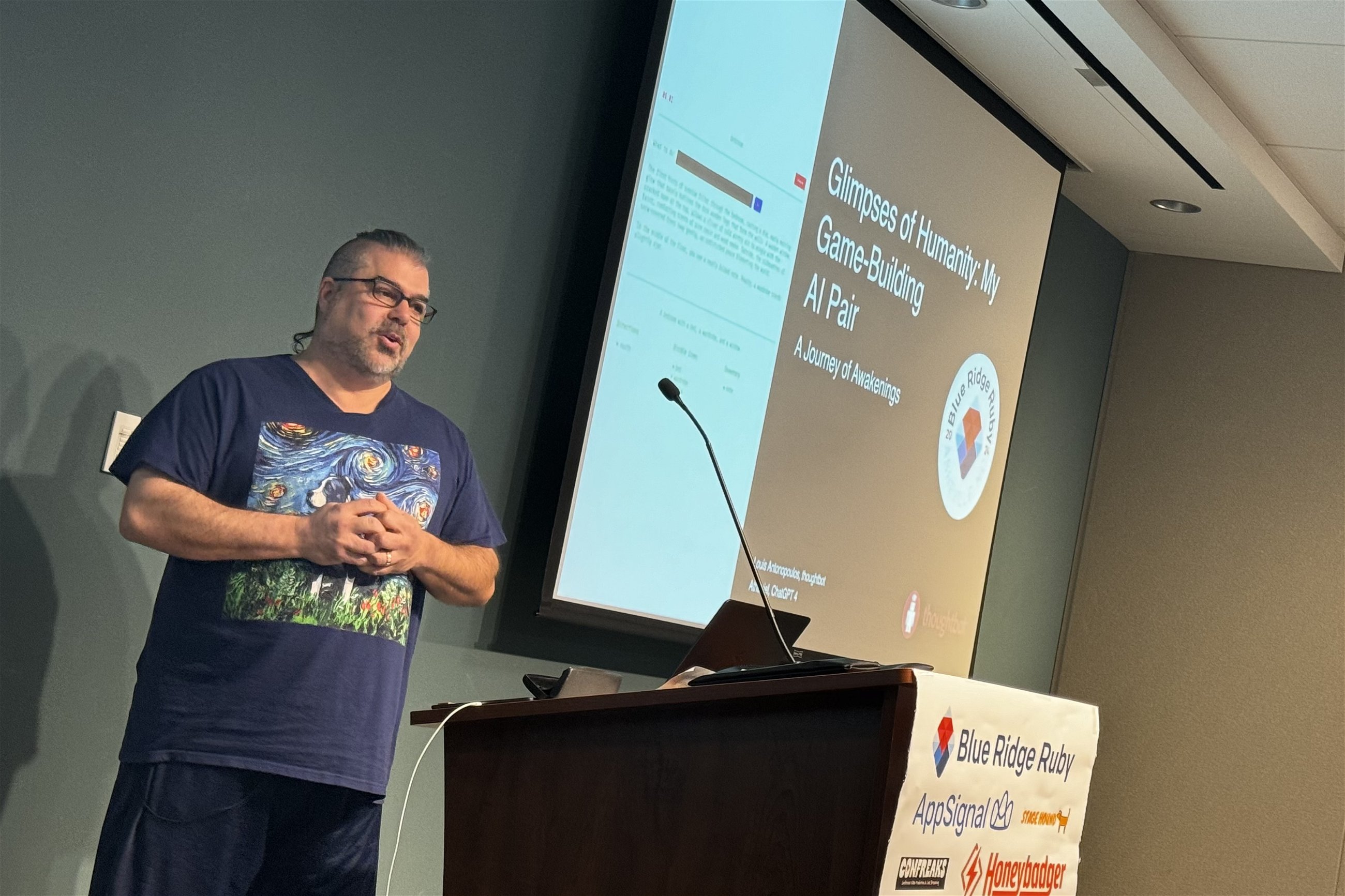 Louis Antonopoulos presents at Blue Ridge Ruby conference on "Glimpses of Humanity: My Game-Building AI Pair," wearing a shirt with a Van Gogh-inspired design, addressing an audience with a slide displayed behind him.