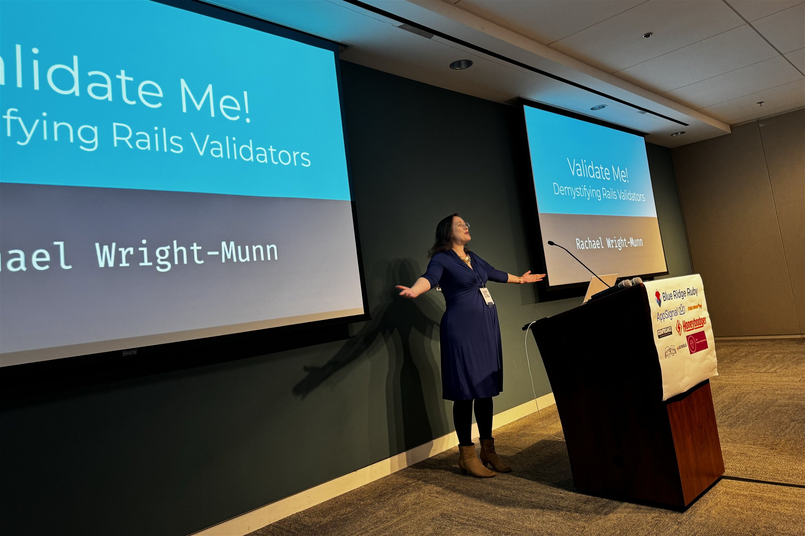 Rachael Wright-Munn presents on "Validate Me! Demystifying Rails Validators" at Blue Ridge Ruby conference, gesturing expressively while addressing the audience, with the presentation title displayed on the screen behind her.